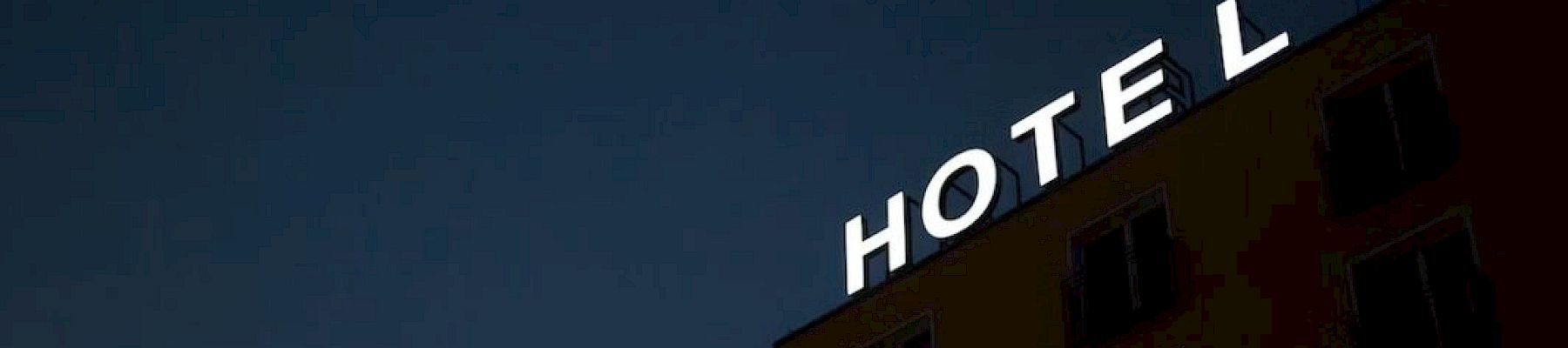 A building at dusk with an illuminated "HOTEL" sign on its roof against a dark sky.