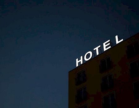 A building at dusk with an illuminated "HOTEL" sign on its roof against a dark sky.
