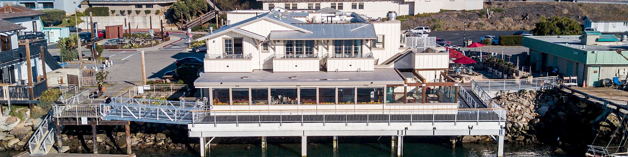 A waterfront building on stilts extends over the water, with houses and other buildings visible in the background.