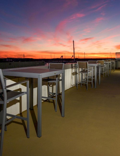 Outdoor seating area with tables and chairs, overlooking a stunning sunset sky.