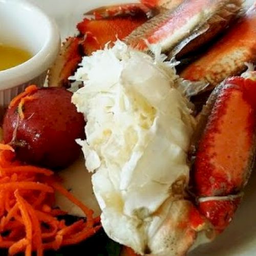 A plate featuring crab legs, melted butter, a slice of lemon, shredded carrots, and a small red potato.