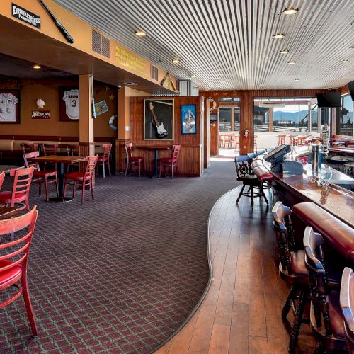 The image shows a bar and restaurant with red chairs, sports decor on the walls, and a view of a marina outside the windows.