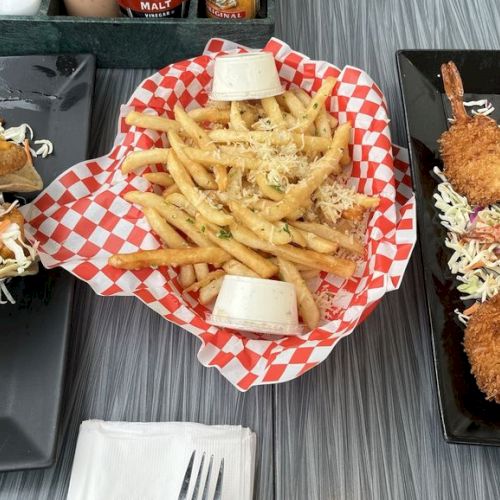 The image shows fried fish tacos with slaw, seasoned fries with sauce, and breaded shrimp with dip, all served on black plates.