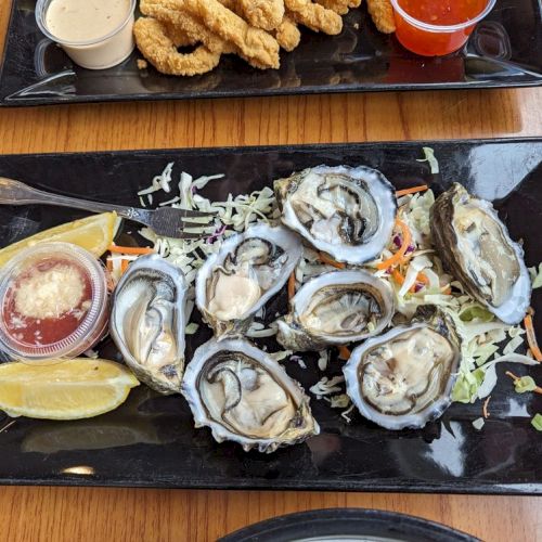 A platter of oysters on a bed of shredded vegetables with lemon wedges and dipping sauce on the side.