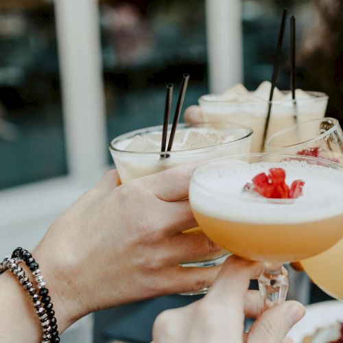 People are clinking glasses filled with cocktails garnished with fruit, likely celebrating or enjoying a gathering together.