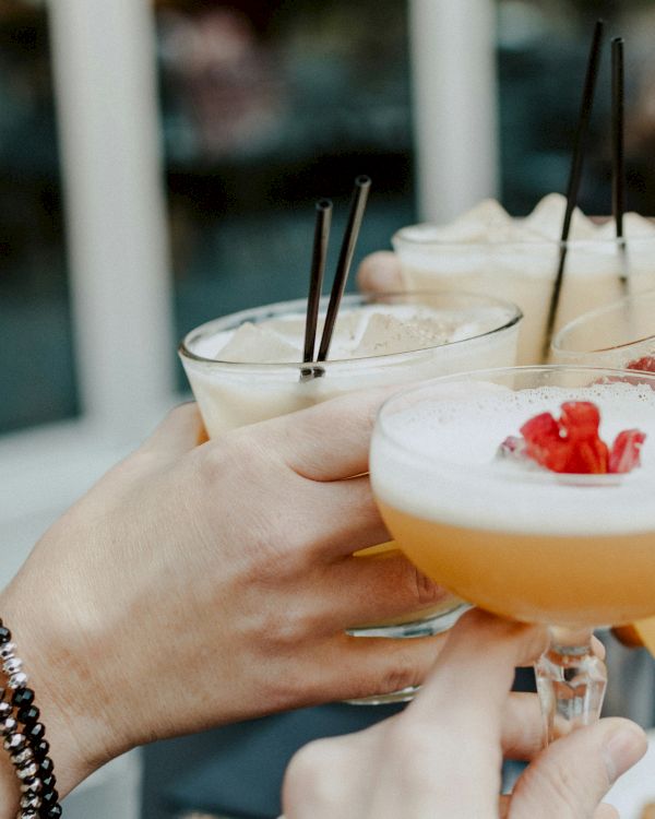 People are clinking glasses filled with cocktails garnished with fruit, likely celebrating or enjoying a gathering together.